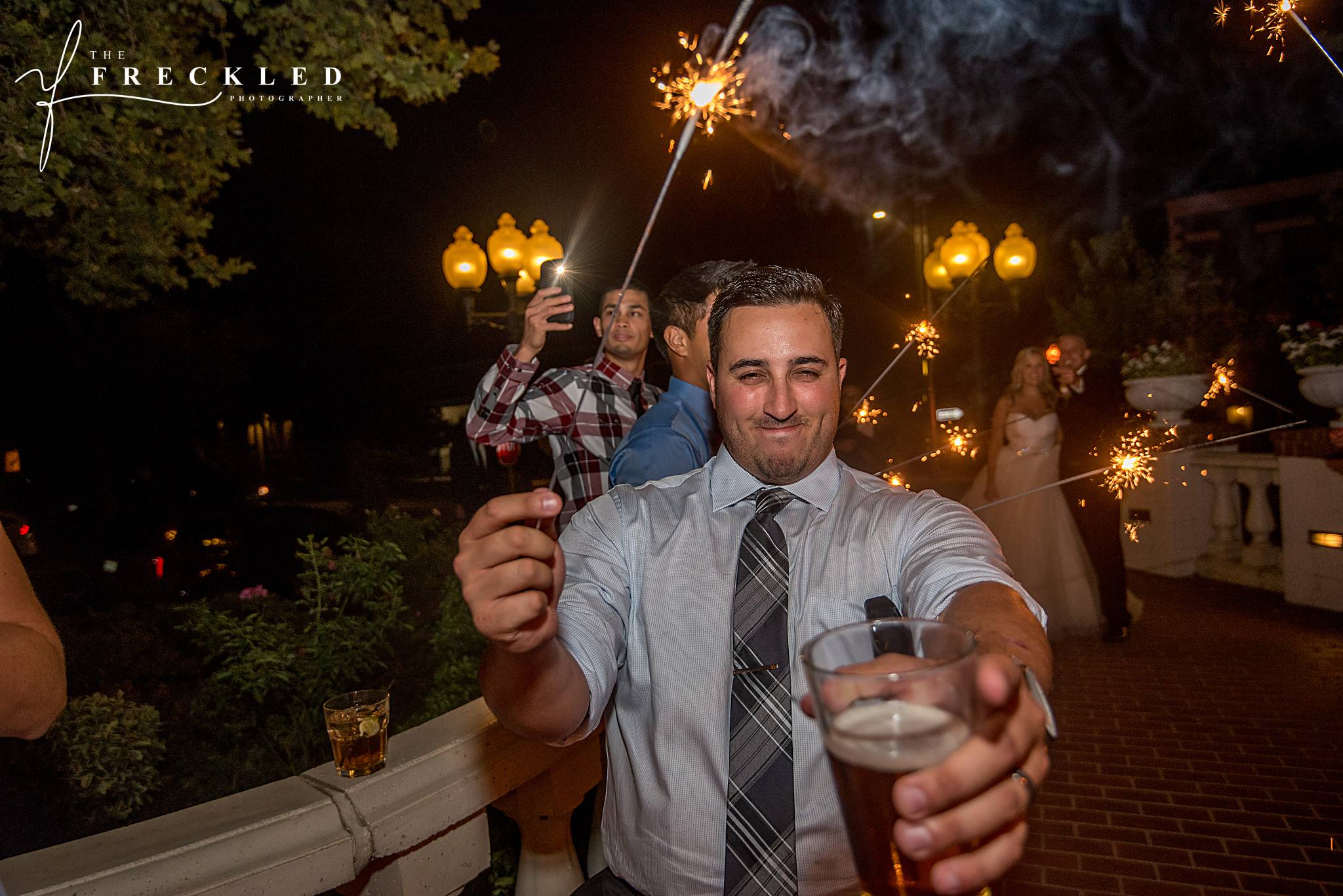 wedding guest holds sparkler in one hand and drink in the other